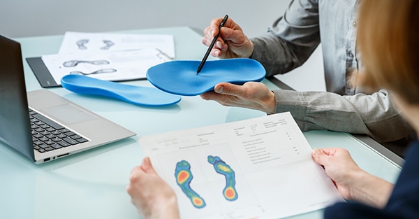 A person holding an orthotic insole in Dublin above a table with foot pressure distribution charts and a laptop. | FCE Scan