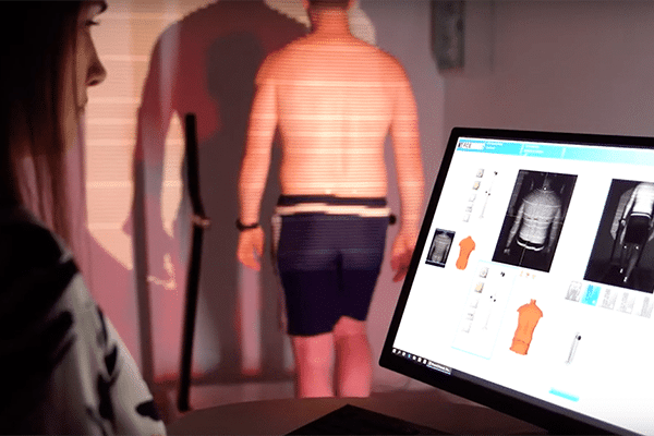 Woman reviews 3D body scan on a computer screen for a Formetric Clinical Evaluation with a subject standing in the background. | FCE Scan